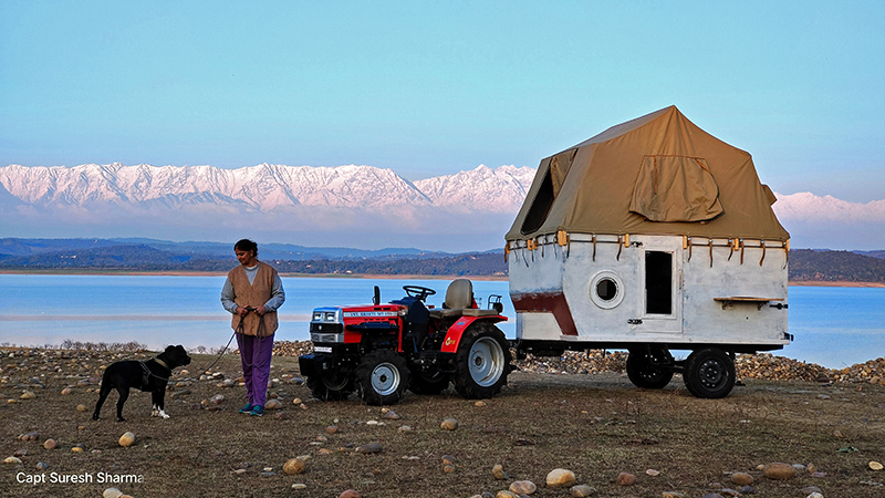 single woman traveller with her pet enjoying vacation around pong dam with carava trailer at offbeat locations holidays with campervan himachal pradesh.