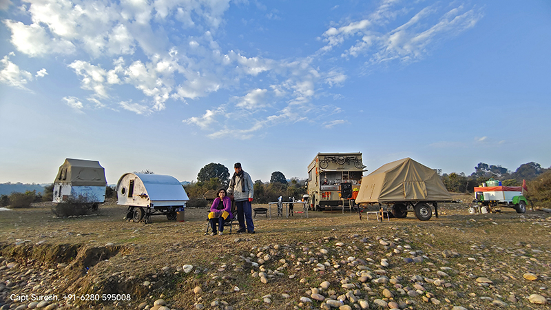 a couple enjoying offbeat soft adventure glamping with caravan motorhome campervan in wilderness himachal for outdoor nomadic camp with social distancing around pong dam in himachal pradesh. 