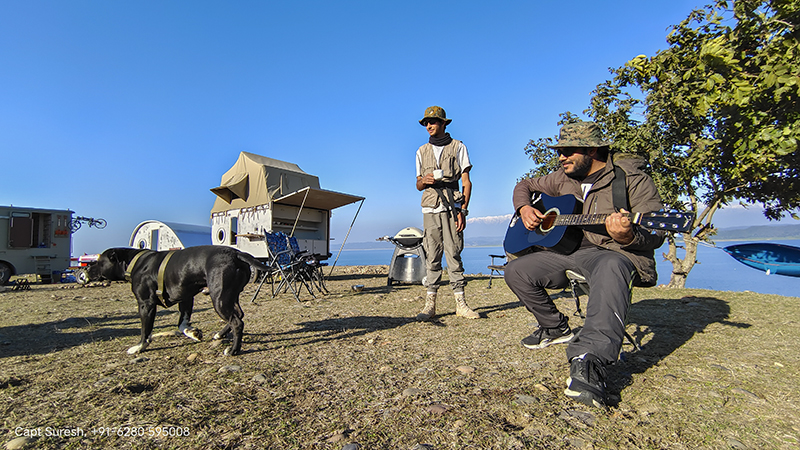 Young boys on offbeat soft adventure holidays with caravan camping trailers while playing musical instrument.